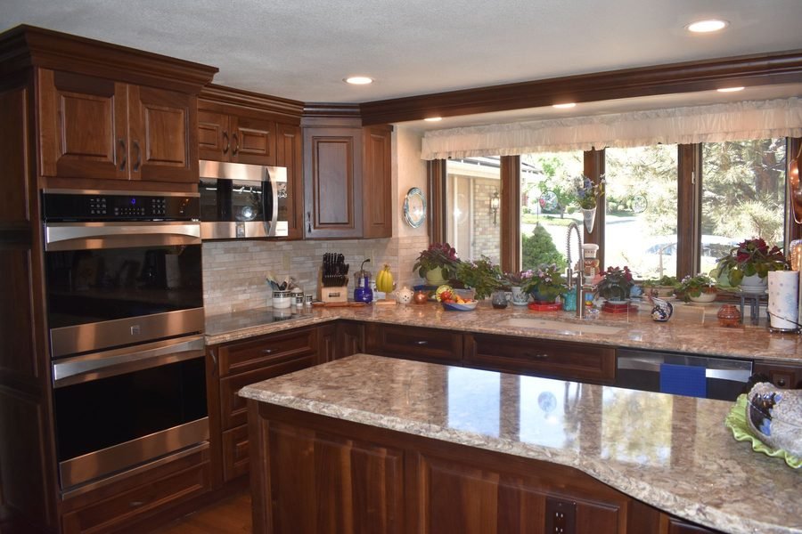A finished kitchen with cherry raised panel cabinets, granite counters, stainless double wall ovens, a curved granite island and undercabinet lighting along a run of windows