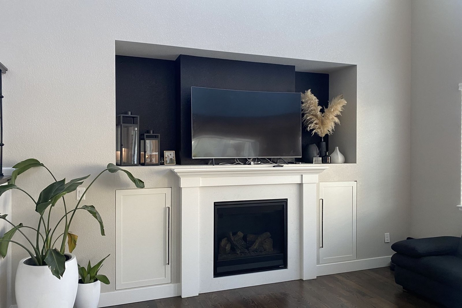 A finished living area fireplace wall: a white painted mantel and surround flanked by cabinets, with a dark painted niche above holding a television