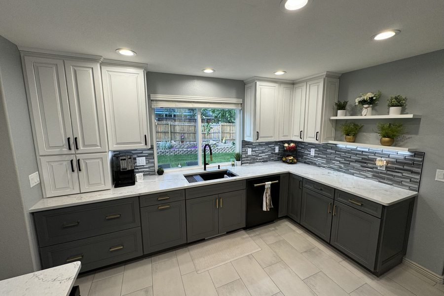 A finished two-tone kitchen: cream upper cabinets, charcoal base cabinets, white stone counters, a black undermount sink and a grey glass tile backsplash
