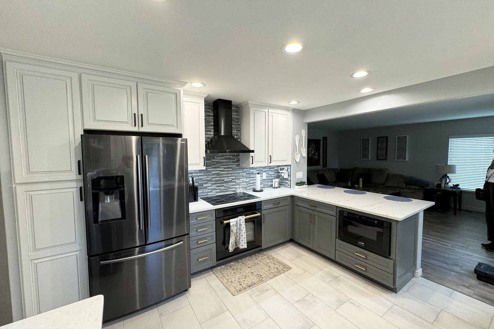 The same two-tone kitchen seen from the other end, with a stainless chimney hood above the range and an island in matching stone
