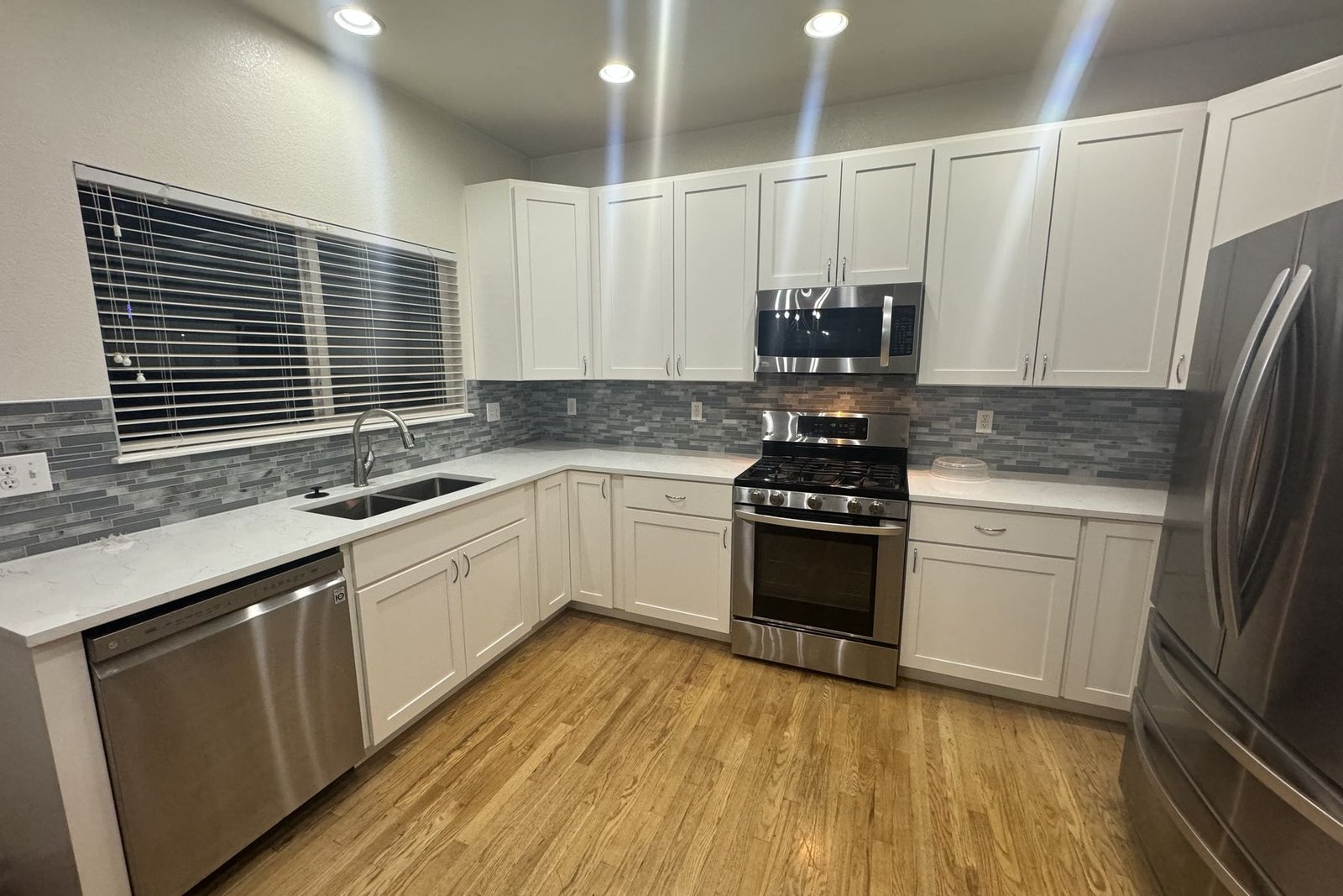 A white kitchen with a dark island, a black and brass hood over the range and stools along the island