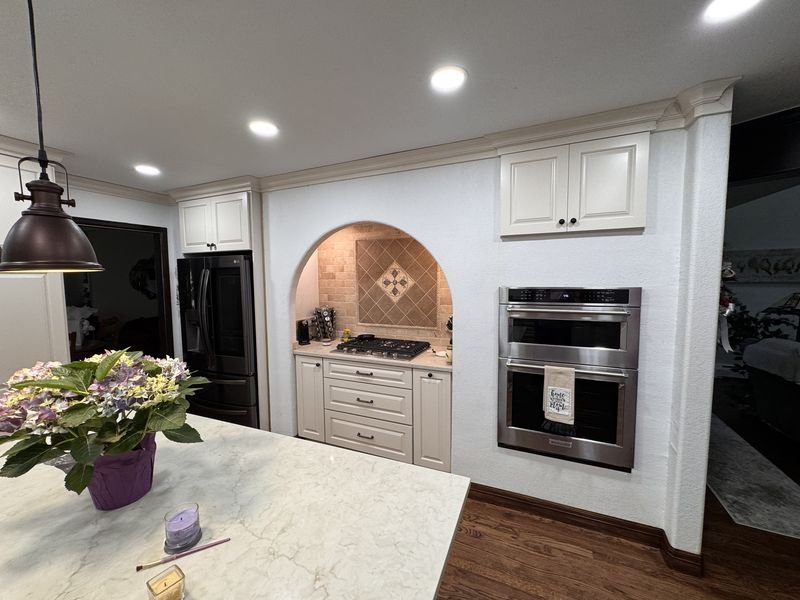 The same arched niche after: cream painted cabinets, a light countertop and a stainless wall oven alongside the arch