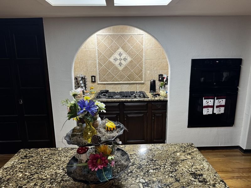 Kitchen before: dark cherry cabinets and heavily patterned dark granite around an arched tiled cooktop niche