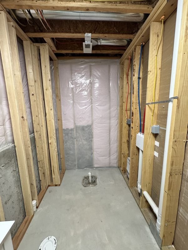 Basement bathroom before: bare stud walls, vapour barrier, a concrete floor and rough-in plumbing