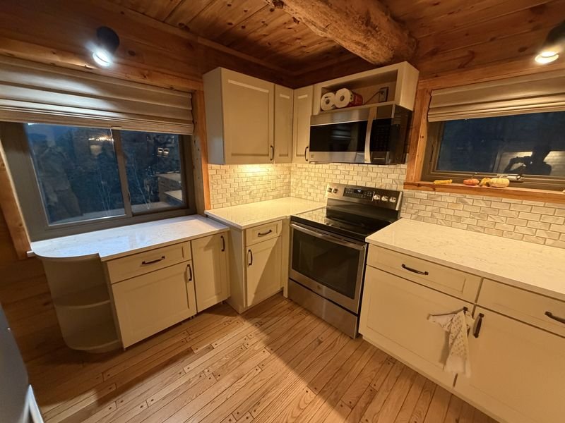 The same log home kitchen after: painted shaker cabinets and a light countertop with the log walls and beamed ceiling kept