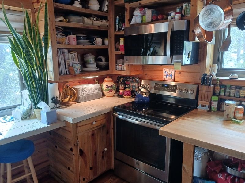 Log home kitchen before: knotty pine cabinetry and butcher block counters under a log ceiling