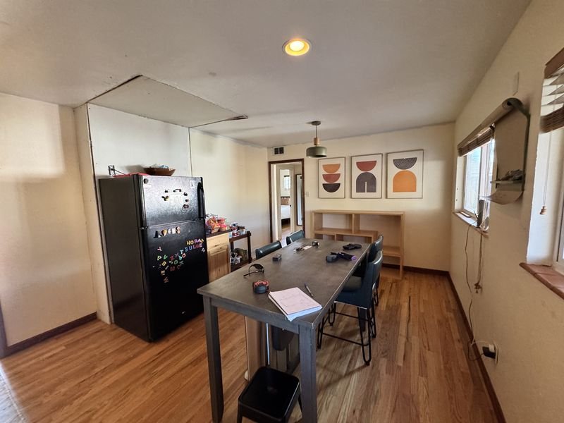 Kitchen wall before: a black top-freezer refrigerator and a low wood cabinet against a partition wall, with an unfinished patch in the ceiling above