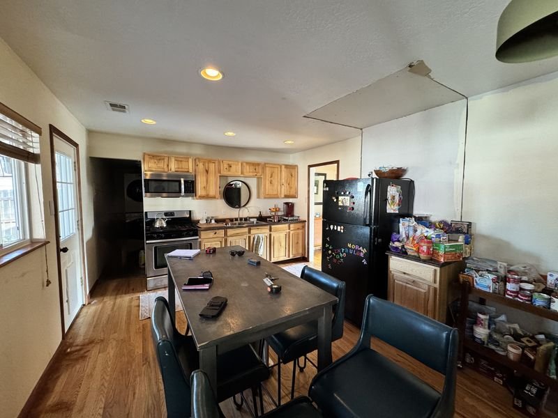 Kitchen before: hickory raised-panel cabinets, a dark laminate counter, a black top-freezer refrigerator and a dining table in the middle of the room