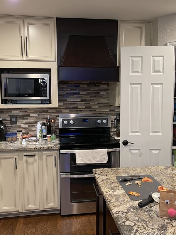 Kitchen range wall before: cream cabinets, an over-range microwave and a mosaic tile strip backsplash