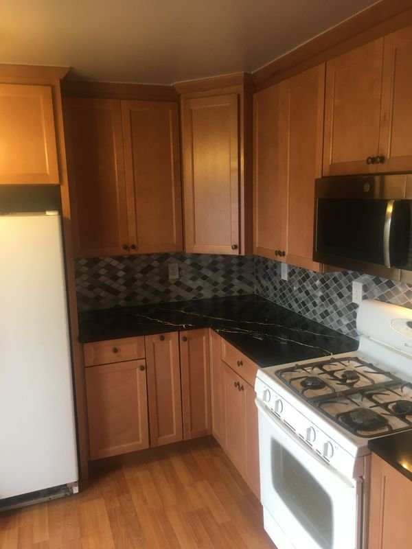 The same kitchen after: maple cabinetry, a dark countertop and a mosaic tile backsplash