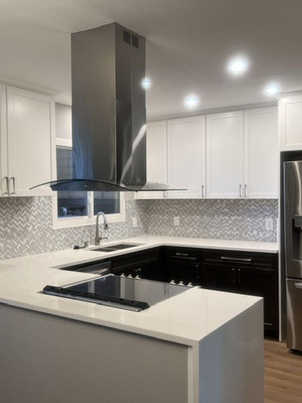 The same kitchen after: full-height white cabinets, an island hood and a light countertop