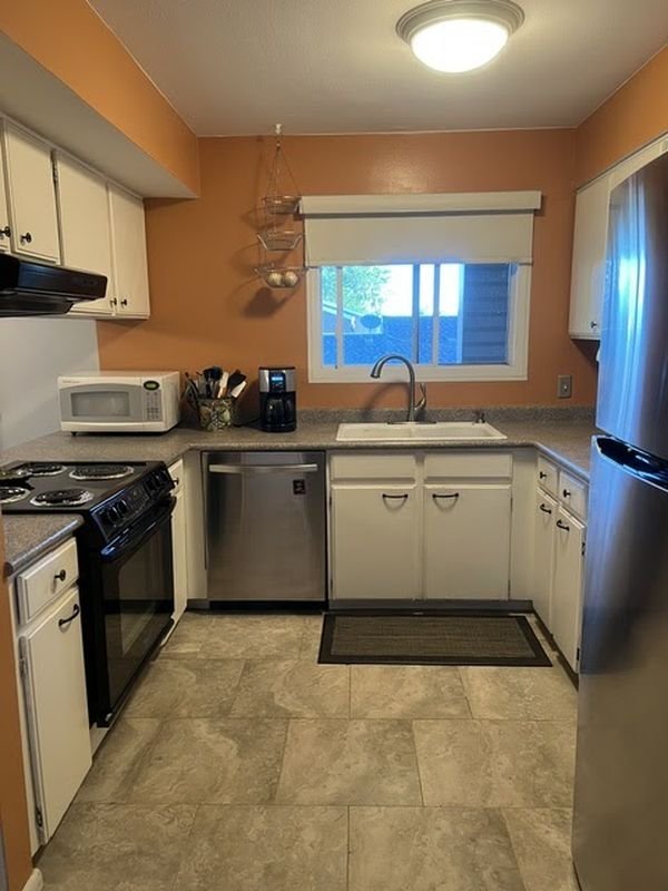 Kitchen before: cream cabinets against orange walls with tile flooring and black appliances