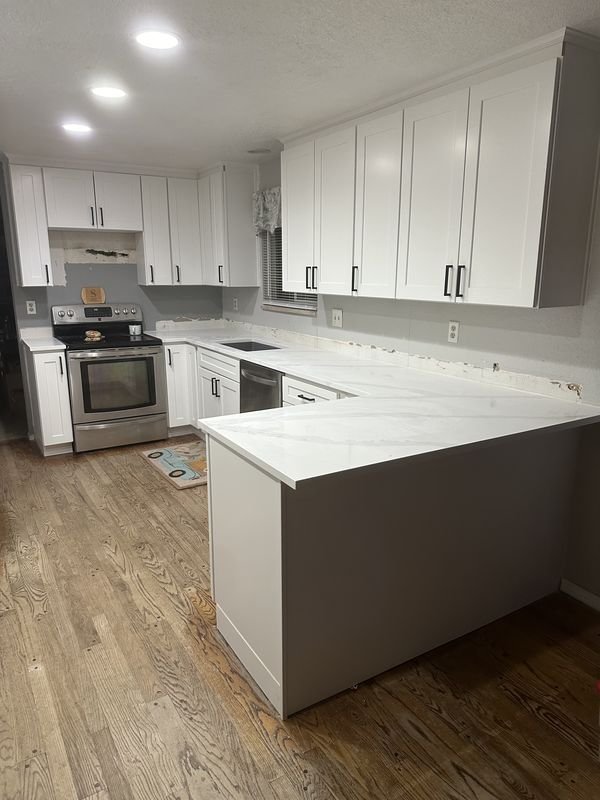 The same kitchen after: white shaker cabinets and a bold-veined stone counter wrapping the peninsula