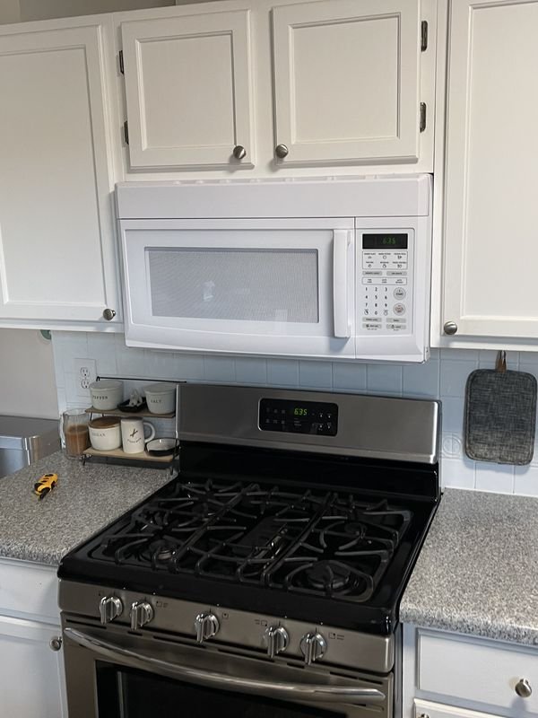 Kitchen range wall before: white raised-panel cabinets, a white over-the-range microwave, a freestanding gas range and a speckled laminate countertop