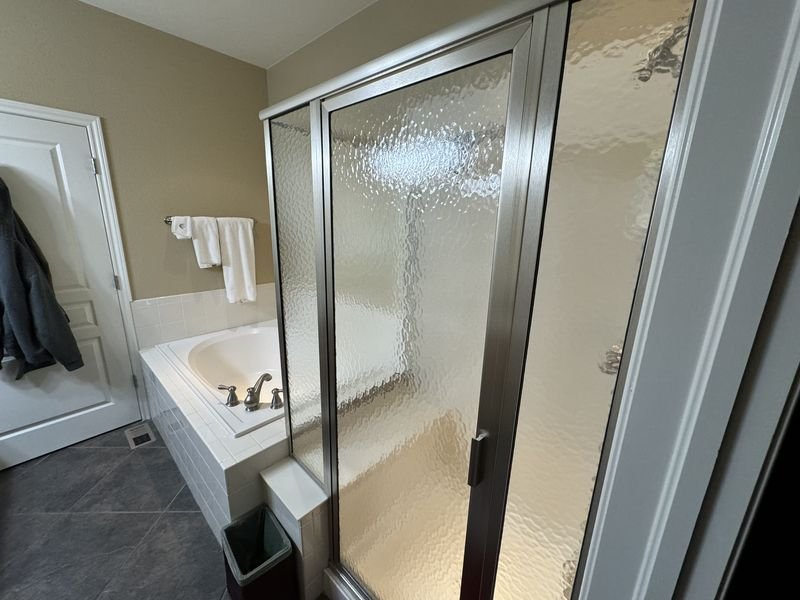 Bathroom before: a drop-in tub in a tiled deck beside a framed glass shower with textured panels