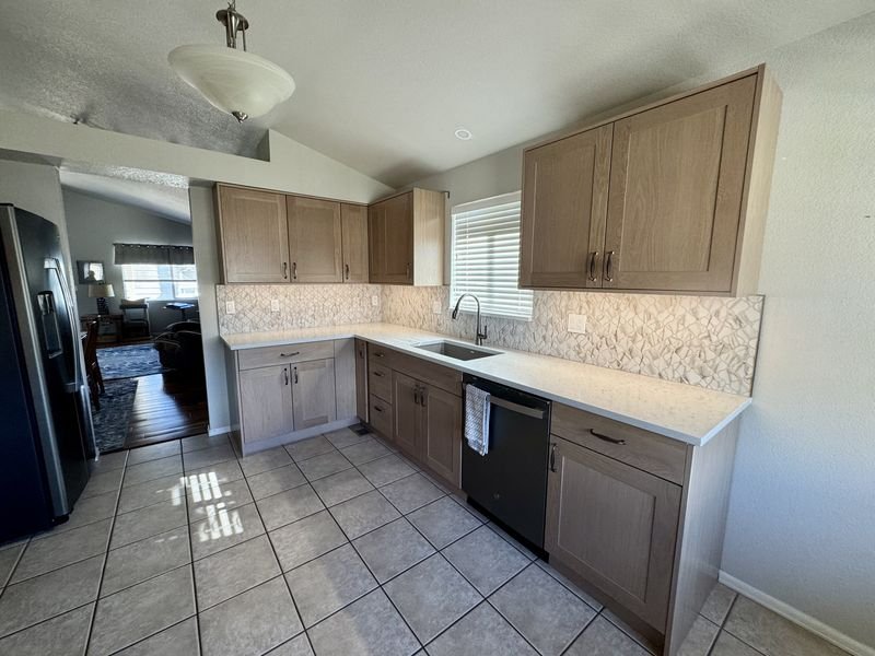 The same kitchen after: light stained cabinets and a pale countertop under the same vaulted ceiling