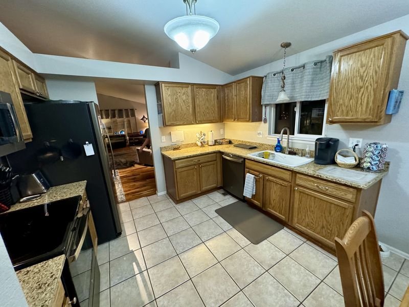 Kitchen before: honey oak cabinets and tile flooring beneath a vaulted ceiling with a pendant light