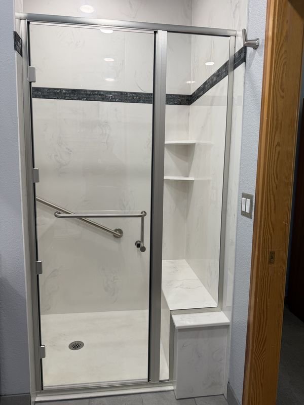 The same shower after: a low-threshold shower with a bright surround, corner seat, grab bar and hand shower
