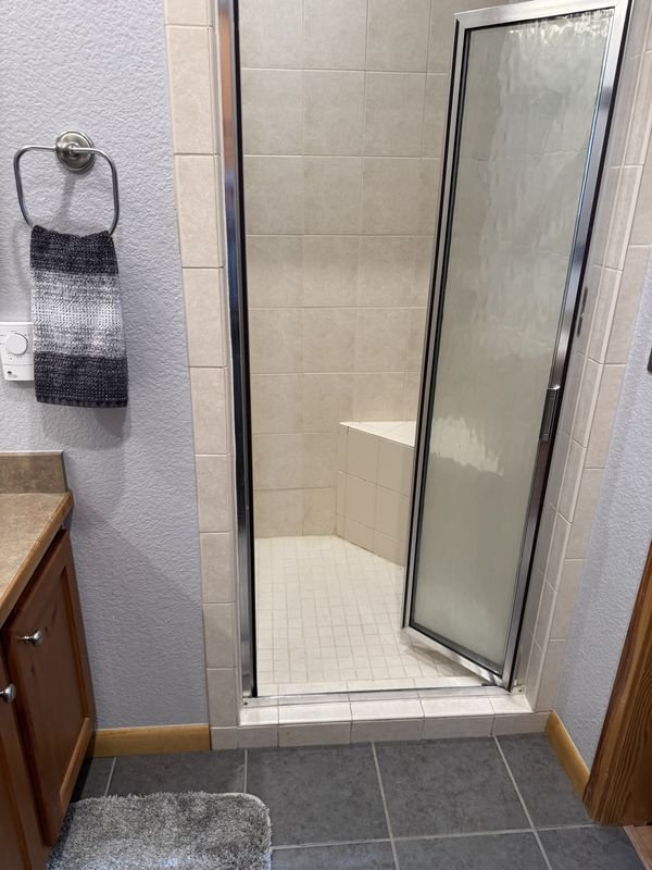 Shower before: a framed glass door with a tiled curb, beige tile and oak trim