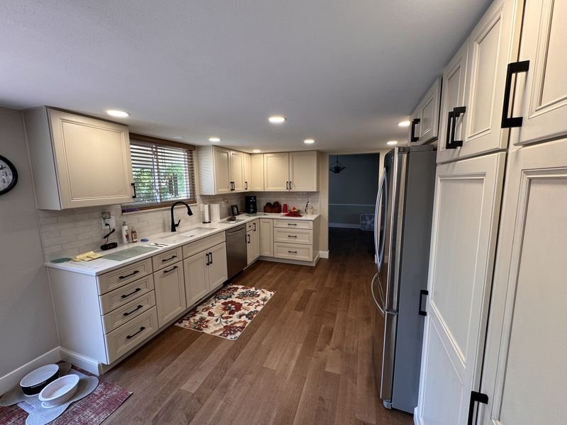The same kitchen after: white cabinets, a light countertop, recessed lighting and wood flooring