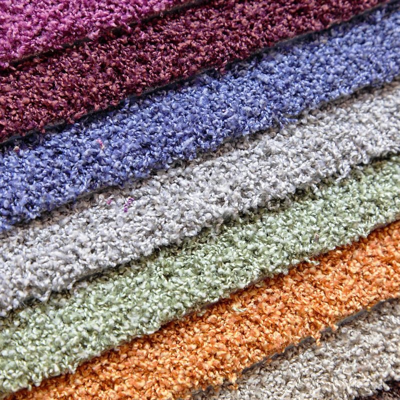 A stack of carpet samples in six colours, close enough to read the pile