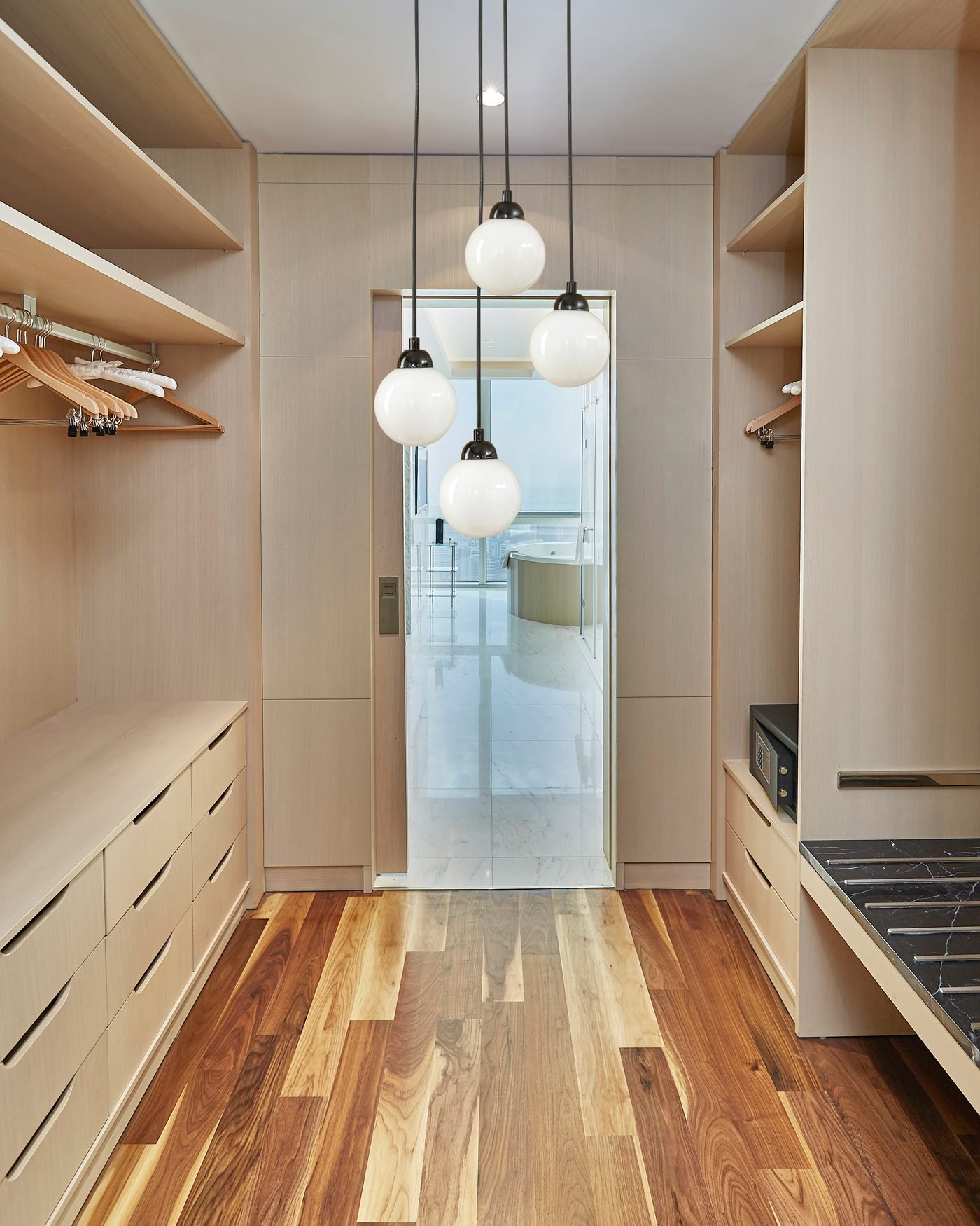 A walk in closet with hanging rails, drawer banks and open shelving down both sides, lit from above