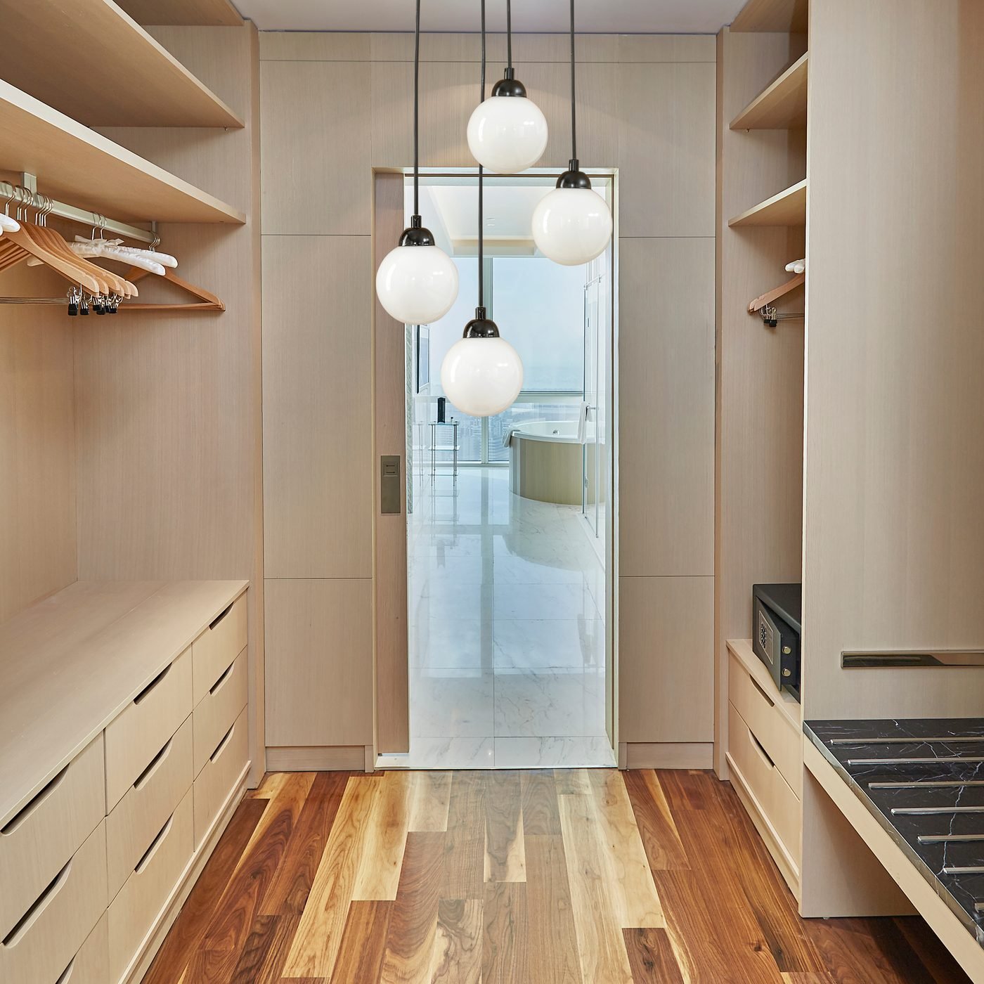 A walk in closet with hanging rails, drawer banks and open shelving down both sides, lit from above