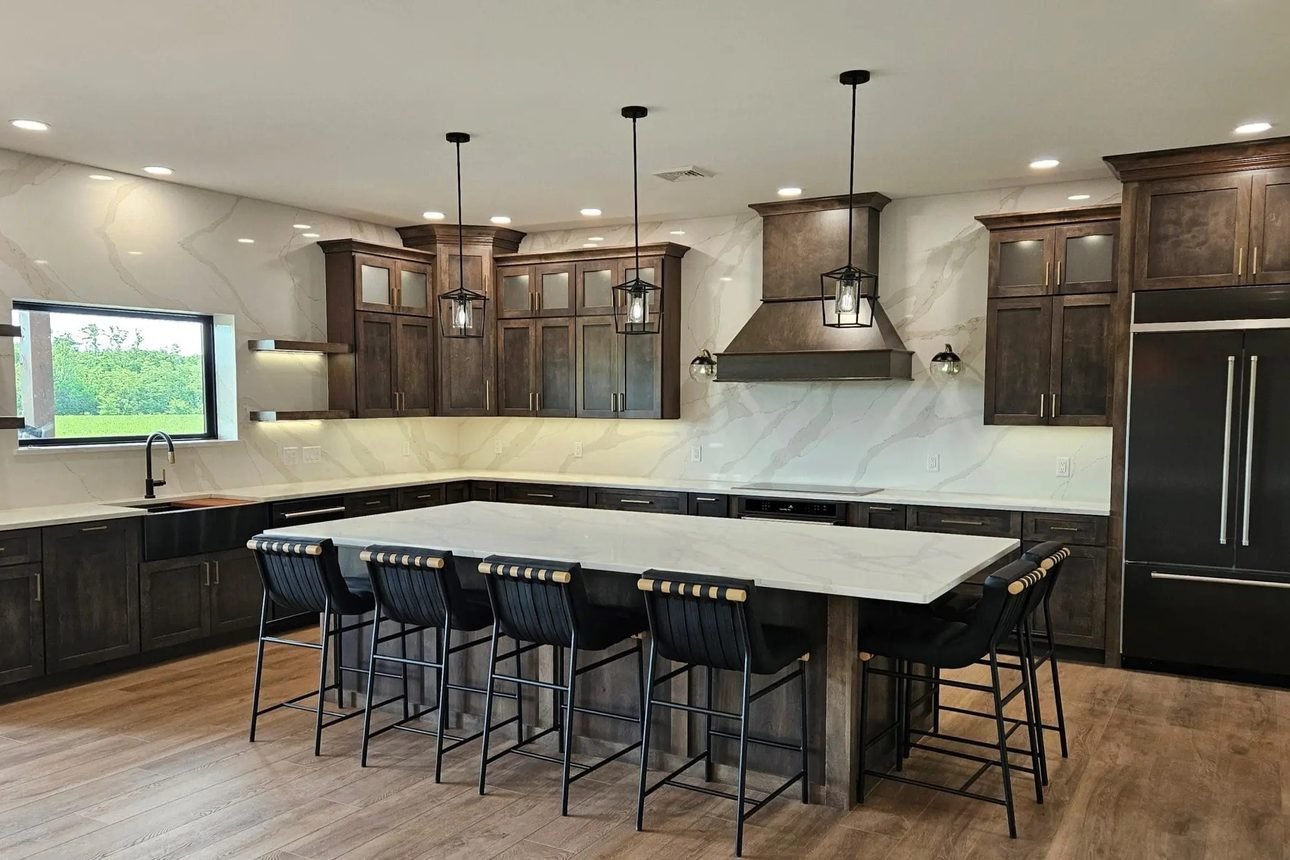 A kitchen in dark stained cabinetry with a white quartz island seating six, a matching quartz slab backsplash running the full wall, and lantern pendants