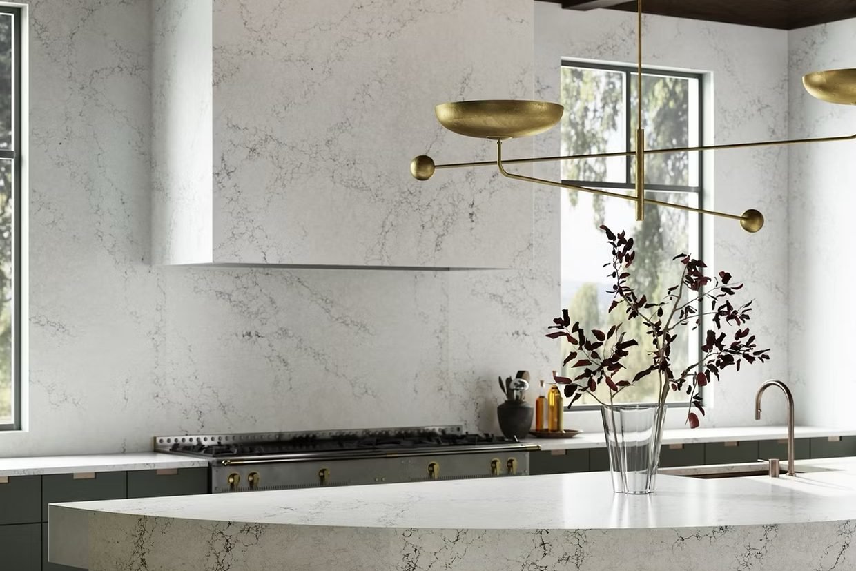 A kitchen in softly veined white quartz carried up the hood and the whole backsplash, with a curved island and a brass chandelier