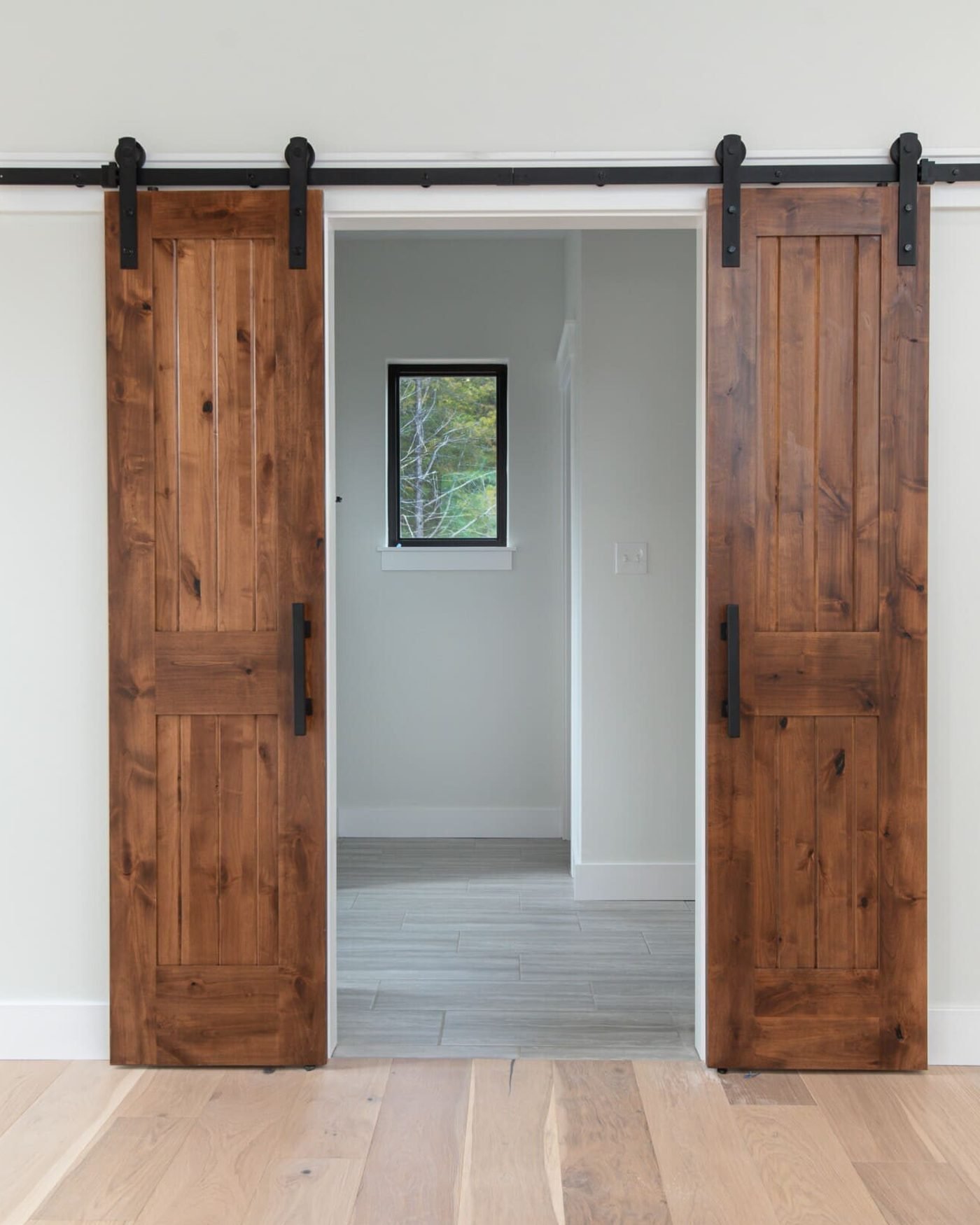 Two stained knotty alder barn doors hung on a black steel track, slid open either side of a doorway, over wide plank oak floors