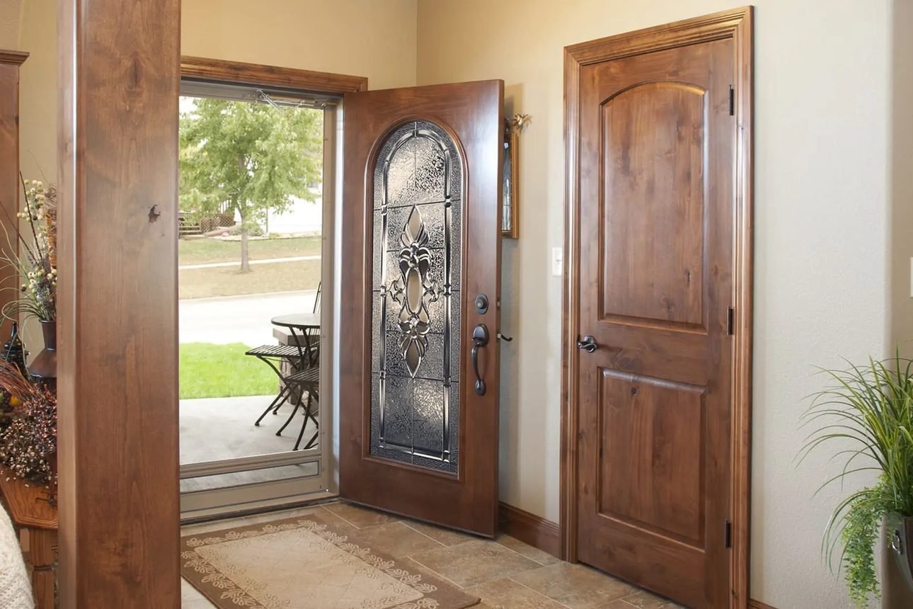A stained wood front door with a tall arched decorative glass panel, standing open beside a matching arch-top interior door on a tiled entry