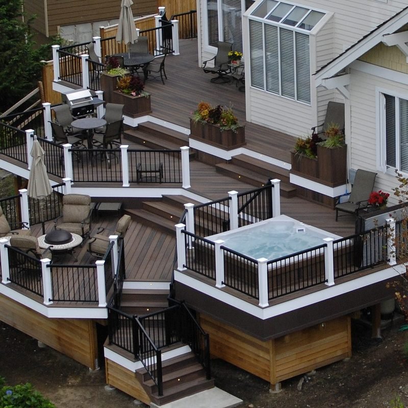 A multi level deck with white railings and steps wrapping the back of a house, with a hot tub on the upper level