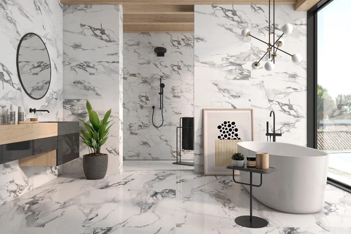 A bathroom tiled floor to ceiling in white and grey marble-look porcelain, with a hexagon tiled shower alcove, a freestanding oval tub, a wood and glass floating vanity and a round mirror