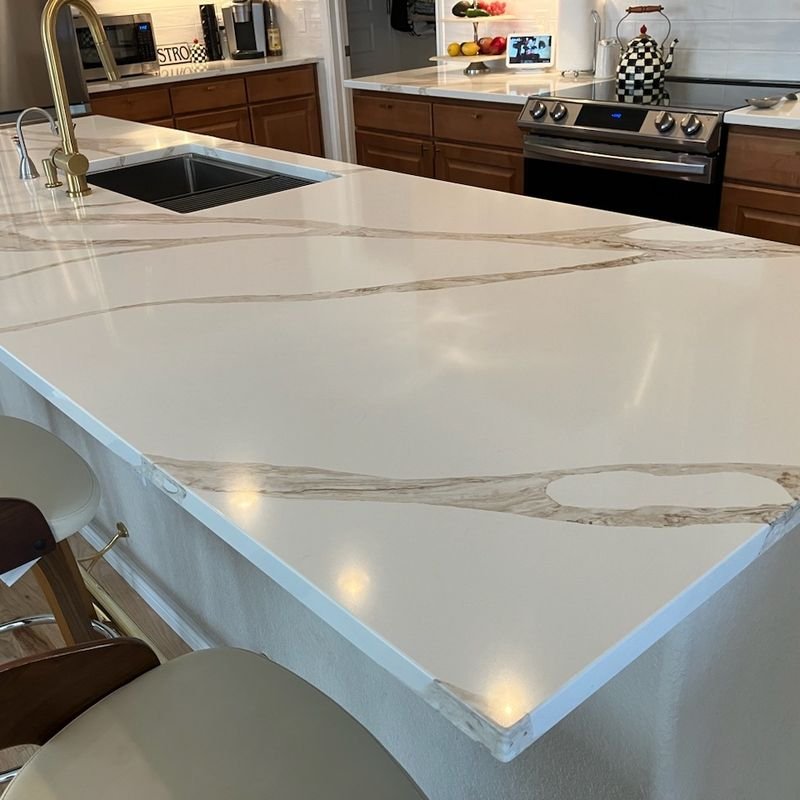 A white quartz island with grey and gold veining, a black undermount sink and a brushed gold faucet