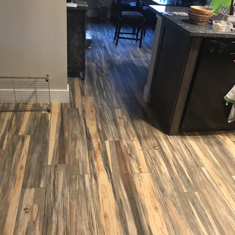 Wood-look plank flooring in mixed warm and grey tones running past a dark kitchen island