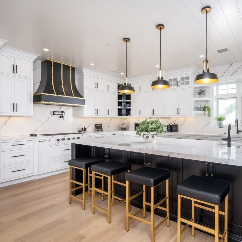 A white kitchen with a dark island, a black and brass hood over the range and stools along the island