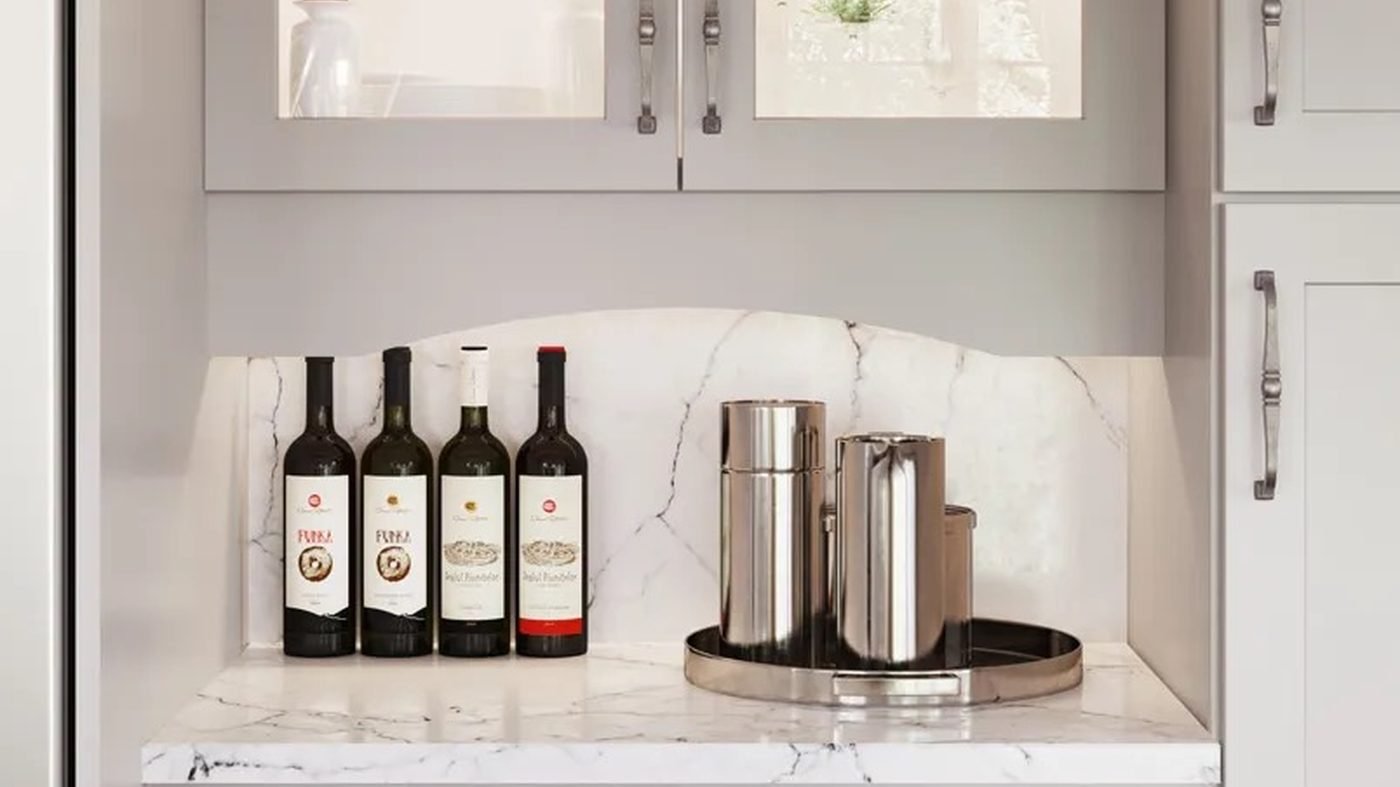 A lit glass-front wall cabinet above a marble bar niche, with four wine bottles and two polished steel canisters on a round tray