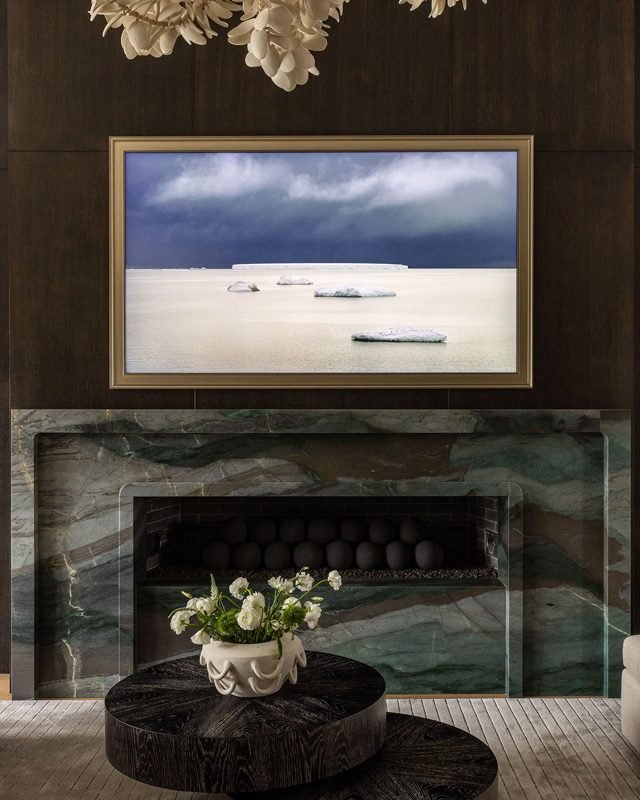 A dark living room with a green marble fireplace, a framed picture above it and a round wood coffee table in front