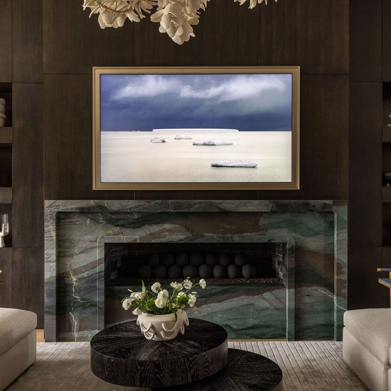 A dark living room with a green marble fireplace, a framed picture above it and a round wood coffee table in front