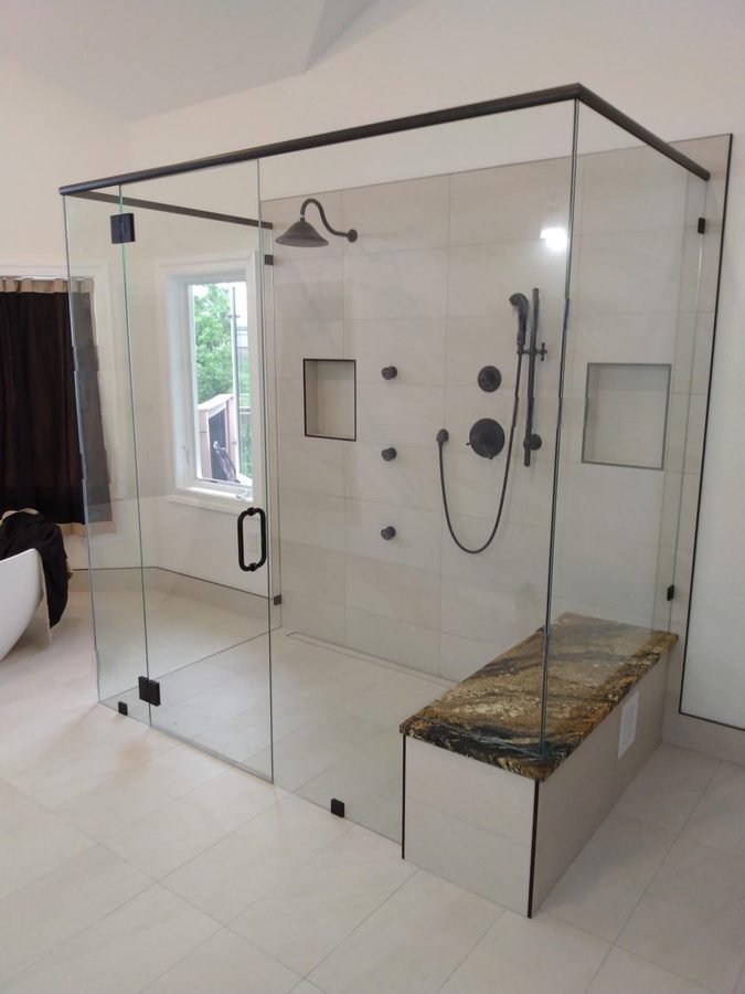 A large glass shower with a bronze frame, body jets, a window and a gold and brown speckled stone bench
