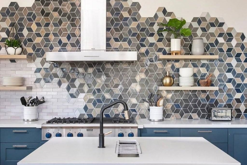 A blue and grey cube patterned mosaic behind a stainless chimney hood and gas range, over white subway tile and navy cabinetry