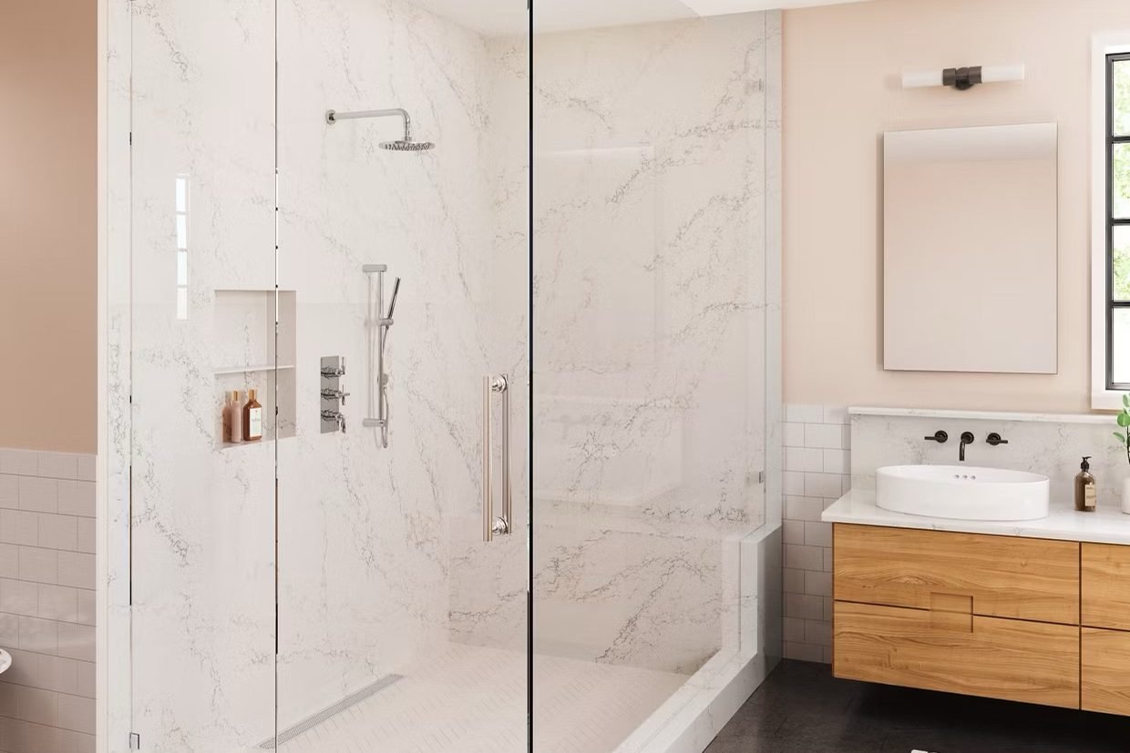 A glass corner shower lined floor to ceiling in softly veined white stone, with a built-in bench and niche, beside an oak floating vanity