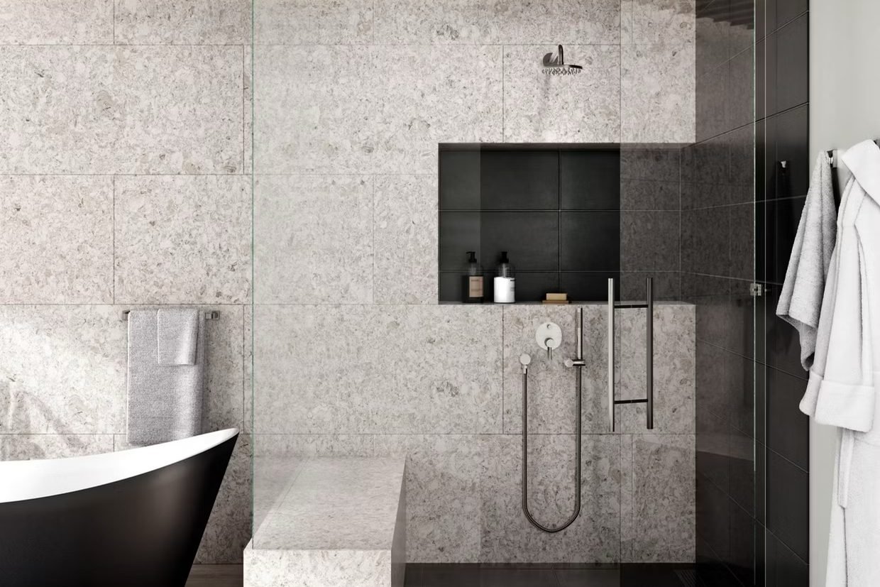 A walk-in shower lined in pale speckled stone with a black tiled niche and black floor, beside a black freestanding tub under a timber ceiling