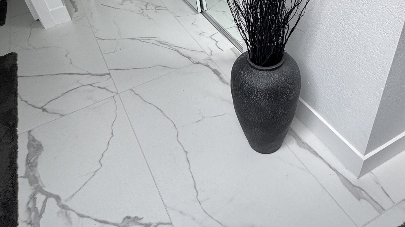 Large-format white marble-look floor tile with soft grey veining, with a dark textured vase against a white wall